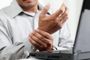 close up of a man's hand in pain in front of laptop