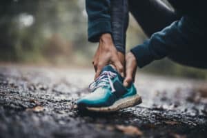 Person holding a painful ankle on a wet running trail, illustrating chronic ankle instability.